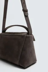 Bolso tipo bandolera fabricado en piel con acabado serraje. Cuenta con compartimento principal con cierre de solapa magnética y cremallera, asa de mano superior y asa de hombro ajustable.