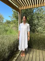 Vestido camisero largo de lino blanco, con cuello camisero, manga corta enrollada y cierre frontal de botones de nácar. Presenta aberturas laterales en el bajo.