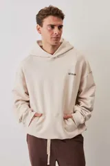 Hoodie de felpa color beige, con capucha, bolsillo frontal tipo canguro y pequeño logo de la marca estampado en el pecho.