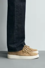 Zapatillas de cordones color beige, fabricadas en piel con acabado serraje. Presentan detalles de pespuntes en la parte superior y suela plana a contraste color crema.