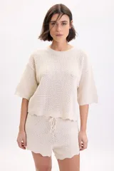 Sweater color crudo de manga corta, confeccionado en tejido de punto con diseño de textura fantasía, cuello redondo y corte holgado.