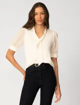 Blusa de color blanco con escote en V y detalle de lazo frontal. Presenta mangas cortas de gasa con terminación en puño.