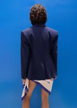 Blazer azul marino de estilo sastrero, corte recto, con cuello pico y solapas de muesca. Cuenta con dos bolsillos con solapa en los laterales y cierre frontal de doble botonadura.
