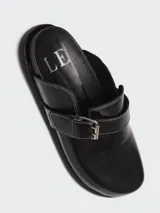 Zuecos de cuero color suela con diseño de punta redonda y ajuste mediante una tira con hebilla metálica en el empeine. Presentan una suela plana de goma negra y plantilla interior con logo grabado.