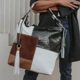 Bolso tipo hobo de cuero vacuno con diseño patchwork en blanco, marrón y negro con textura de cocodrilo. Tiene correa corta de mano y correa larga ajustable para usar como morral.