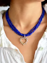 Collar de tres vueltas compuesto por pequeñas cuentas de vidrio en color azul intenso, con un dije central en forma de corazón con diseño de rayos en metal plateado.