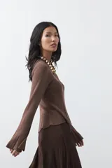 Top de tejido acanalado con sutil acabado metalizado, de silueta entallada con diseño peplum en la cintura y mangas largas levemente acampanadas.