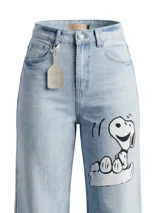 Jean de corte wide leg en denim azul claro con lavado desgastado. Presenta una ilustración pintada a mano de Snoopy en la pierna derecha, acompañada por la palabra 'Real', una corona y una estrella. Incluye etiqueta de cuero en la cintura y en el ruedo.