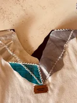 Vestido corto tejido en hilo de algodón color celeste, con cuello y espalda con apliques de cuero artesanal en tonos marrón, blanco y celeste.