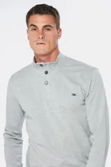 Remera de manga larga tipo buzo liviano, confeccionada en tejido jersey color gris melange. Presenta cuello mao con tapeta de tres botones y puños en rib.