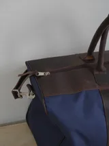 Bolso de lona color verde militar con detalles en cuero marrón. Tiene doble asa de mano y correa de hombro ajustable y extraíble.