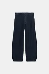 Pantalón de lino azul marino de tiro medio, corte barrel con pierna ancha y silueta abombada. Cuenta con bolsillos laterales ocultos, trabillas en la cintura y cierre frontal con cremallera y botón.