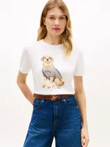 Remera blanca de manga corta Tommy Hilfiger, confeccionada en algodón, con cuello redondo y estampa frontal de un perro golden retriever con suéter a rayas.