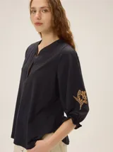 Remera de algodón de color negro con cuello en V y mangas tres cuartos abullonadas, con puños elásticos y detalles de bordado artesanal en las mangas.