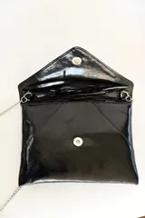 Sobre de mano tipo clutch confeccionado en charol negro brillante con solapa geométrica y cadena metálica plateada delgada.