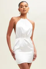 Vestido corto de satén color blanco, con escote halter y detalle de cadena dorada en el cuello. Presenta espalda descubierta y ajuste en la cintura.