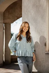 Camisa de algodón a rayas verticales en color verde y blanco, con cuello camisero, mangas largas y un detalle de volado en el ruedo que le otorga una silueta acampanada.