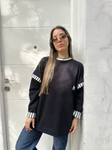 Buzo oversize de color negro con detalles de rayas blancas y negras en el cuello, puños y hombros. Presenta un pequeño parche bordado en el pecho.