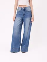 Jean de corte wide leg con diseño de pata ancha y costuras laterales decorativas. Presenta un lavado azul medio con efecto desgastado y ruedo desflecado.