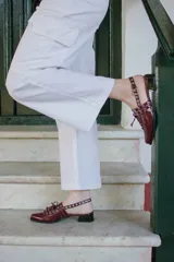 Sueco de cuero color borgoña con cordones, ojales y hebillas plateadas. Tiene tira trasera regulable con elástico.