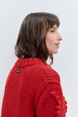 Sweater de punto grueso color rojo, con cuello alto y diseño de relieves tipo pompones en el frente y las mangas. Presenta puños y ruedo acanalados.