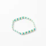 Pulsera elástica compuesta por cuentas rectangulares planas en colores blanco, turquesa y detalles metálicos dorados.