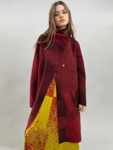 Tapado de lana merino afieltrada con diseño artesanal teñido en tonos rojizos y oscuros. Presenta cuello elevado, cierre frontal con broches ocultos y bolsillos laterales. El diseño es ligeramente más largo en la parte trasera.