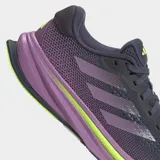 Championes de running Adidas Supernova Rise para mujer, con capellada de malla en tonos gris oscuro y morado, tres franjas moradas y detalles en amarillo neón. La mediasuela es gruesa, predominantemente morada con una capa de amortiguación en amarillo neón que lleva la inscripción "DREAMSTRIKE+".