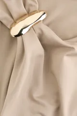Top entallado sin mangas en punto elástico suave, de color beige. Presenta escote asimétrico con detalle metálico en un tirante y frunces laterales que generan un efecto drapeado.
