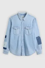 Camisa de jean estilo western con diseño de parches tipo sashiko en las mangas. Presenta cuello clásico, cierre frontal con botones a presión, dos bolsillos en el pecho con solapa y puños abotonados.