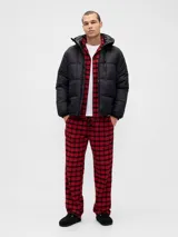 Pijama de hombre compuesto por una camisa de manga larga y un pantalón largo, ambos confeccionados en tela de franela con estampado de cuadros en tonos rojo y negro. La camisa cuenta con cierre frontal de botones y cuello clásico, mientras que el pantalón presenta un corte recto y cómodo.