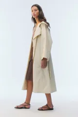 Trench coat oversize color beige, largo, con doble botonadura, solapas amplias, bolsillos laterales y cinturón ajustable para anudar.