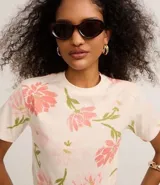 Blusa de corte slim confeccionada en algodón, con cuello redondo y mangas cortas. Presenta un estampado floral en tonos rosados y verdes sobre una base de color crema.