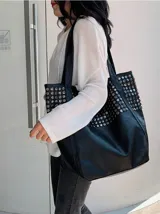 Bolso tote negro de cuero sintético con diseño holgado y dos asas de hombro. Presenta tachas metálicas redondas plateadas cubriendo la parte superior del cuerpo del bolso.