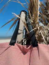 Bolso tipo tote rayado en tonos rosa y blanco, con asas cortas negras y correa larga regulable negra.