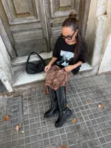 Bota de caña alta estilo biker, confeccionada en cuero sintético negro. Presenta una suela track con plataforma, puntera redondeada y un detalle de arnés con hebilla metálica y tachas en la zona del tobillo.