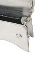 Cartera tipo bandolera pequeña, color plateado metalizado, con solapa superpuesta y correa fina ajustable.