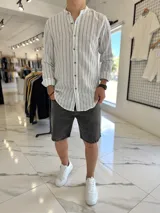 Camisa de lino blanca con rayas verticales negras, cuello mao y cierre frontal con botones marrones.
