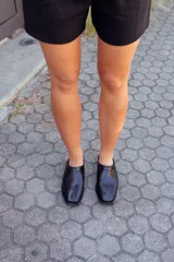 Zapatos tipo mules de cuero negro, con punta fina y detalle de charol en el borde superior.