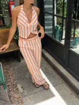 Mono largo a rayas verticales color naranja y blanco, con escote halter y corte ajustado.