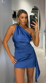 Vestido corto de satén color azul, con diseño de un solo hombro y detalle de frunces laterales que crean un efecto drapeado, finalizando en una caída lateral asimétrica.