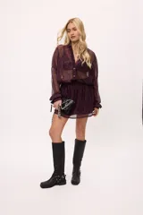 Vestido corto de estilo camisero confeccionado en chiffon con acabado brillante, color bordó. Presenta mangas largas, cuello camisero, cierre frontal con botones y cintura elástica que define la silueta.