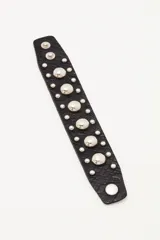 Pulsera de cuero negro con textura grabada, decorada con múltiples tachas metálicas plateadas de diferentes tamaños y cierre con broches a presión.