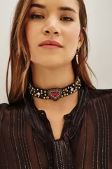 Gargantilla tipo choker de color negro, con apliques de strass y cristales en toda la banda. Presenta un dije central en forma de corazón decorado con piedras rojas y brillantes.
