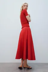 Falda midi de tiro alto y corte en A, color rojo, con bolsillos laterales ocultos y cierre lateral con cremallera.