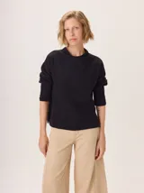 Buzo de lana negro con cuello chimenea y mangas tres cuartos. Presenta un tejido texturado con trenzas en la parte inferior del torso y mangas.