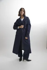 Trench largo de corte oversize en color azul marino, con solapas amplias, cierre frontal de doble botonadura y detalles de trabillas en los hombros y puños.