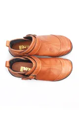 Bota baja de cuero color marrón, estilo botín con elásticos laterales y tira con hebilla metálica ajustable. Cuenta con costuras decorativas pespunteadas y suela de goma con relieve.
