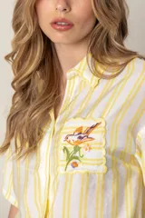 Camisa de mangas cortas con diseño color block en verde, blanco y rosa. Tiene un bolsillo con bordado de ave y flores bordadas en el frente.