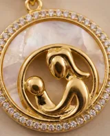 Collar de cadena dorada con dije circular de bronce que presenta una figura de madre e hijo en relieve sobre fondo de nácar, bordeado por incrustaciones de circonia.